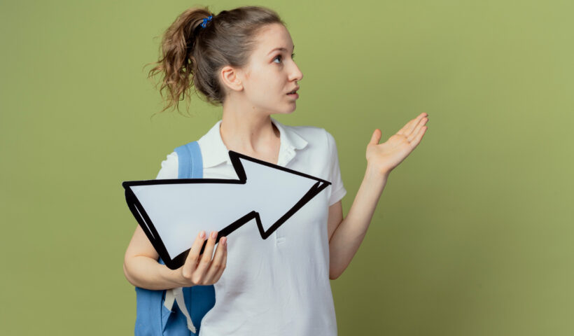 impressed-young-pretty-female-student-wearing-back-bag-holding-arrow-mark-which-is-pointing-side-looking-pointing-side-with-hand-isolated-background-with-copy-space