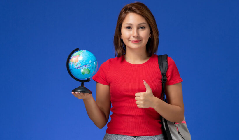 front-view-female-student-red-shirt-with-backpack-holding-little-globe-smiling-blue-wall